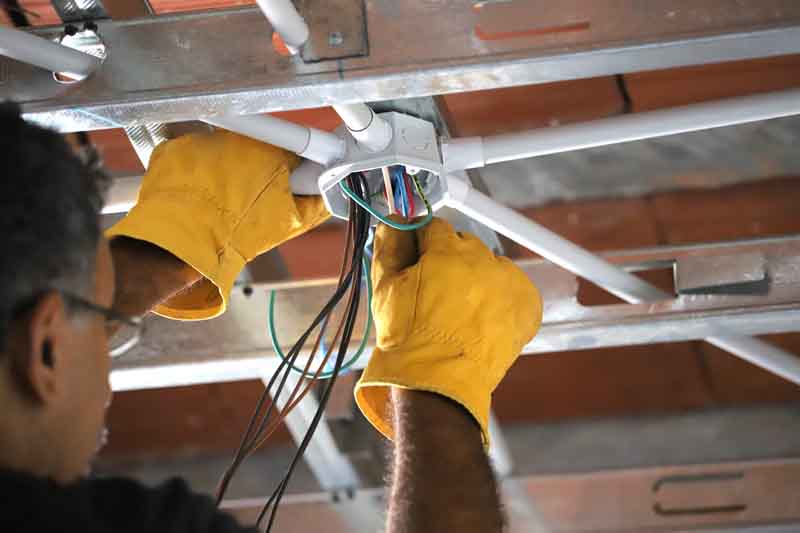 Electrician routing electric wiring through conduit in the ceiling