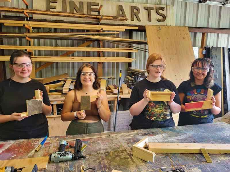 Group of students smiling and working on carpentry set construction