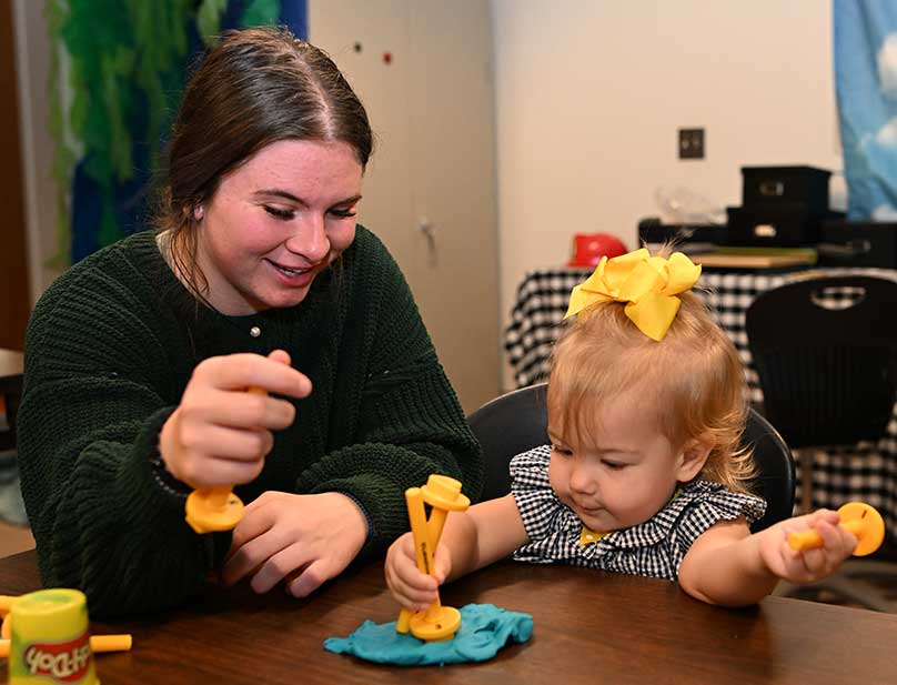 Student and toddler playing together with playdoh