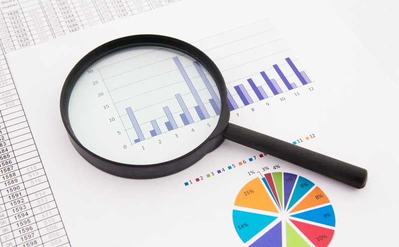 magnifying glass lying on top of a paper showing graphs and statistics
