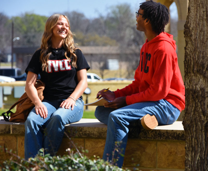 two tvcc students talking outside while sitting on a concrete wall