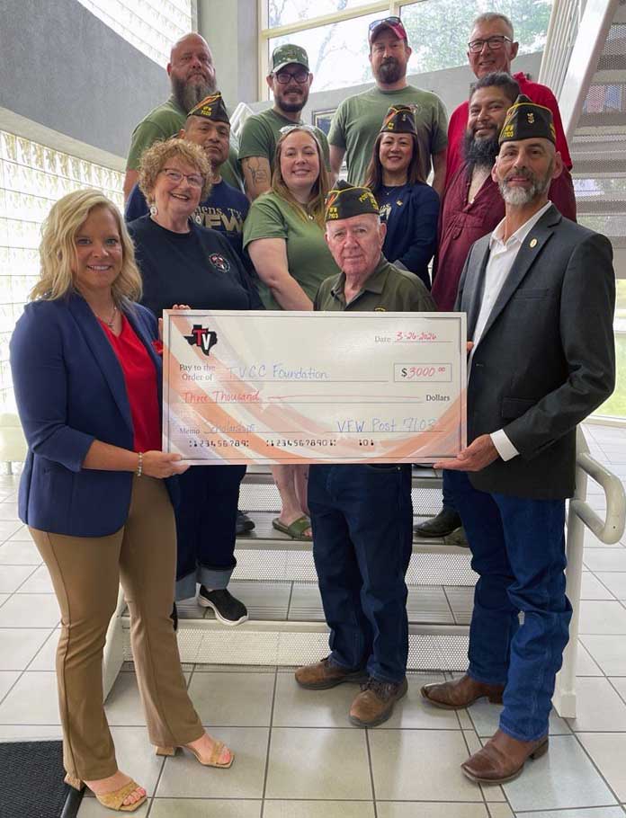 a group of veterans with a foundation member holding a check while standing on a stairway.