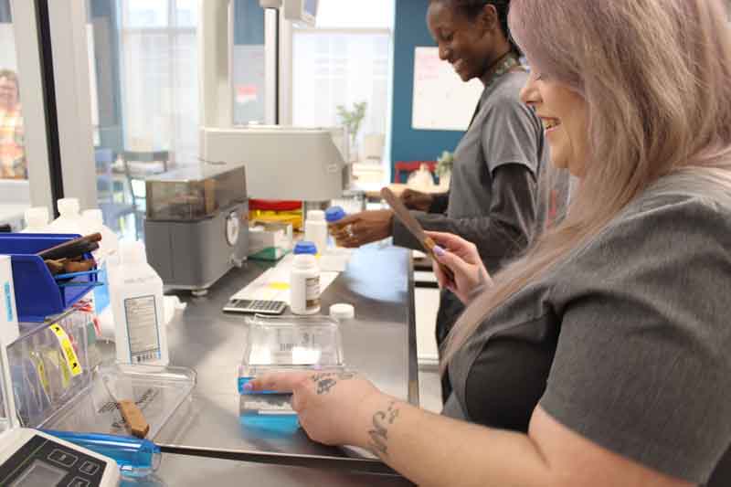 Two female students smiling and working in the pharmacy