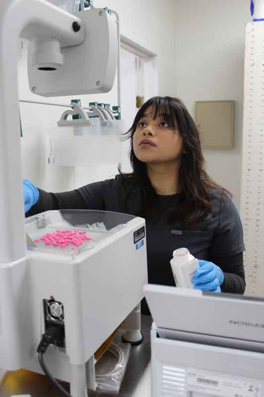 Female pharmacy tech using a machine with pink pills on top of it