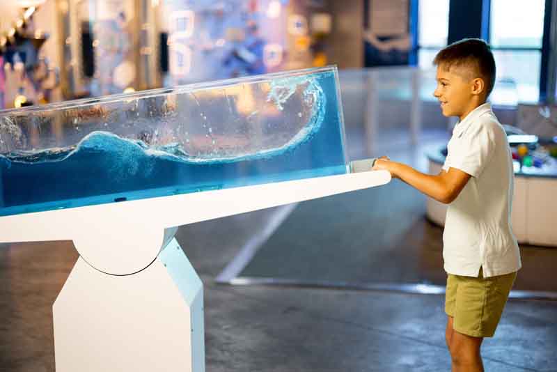 Boy playing with a seesaw that has an enclosed clear box on top of it and filled with water